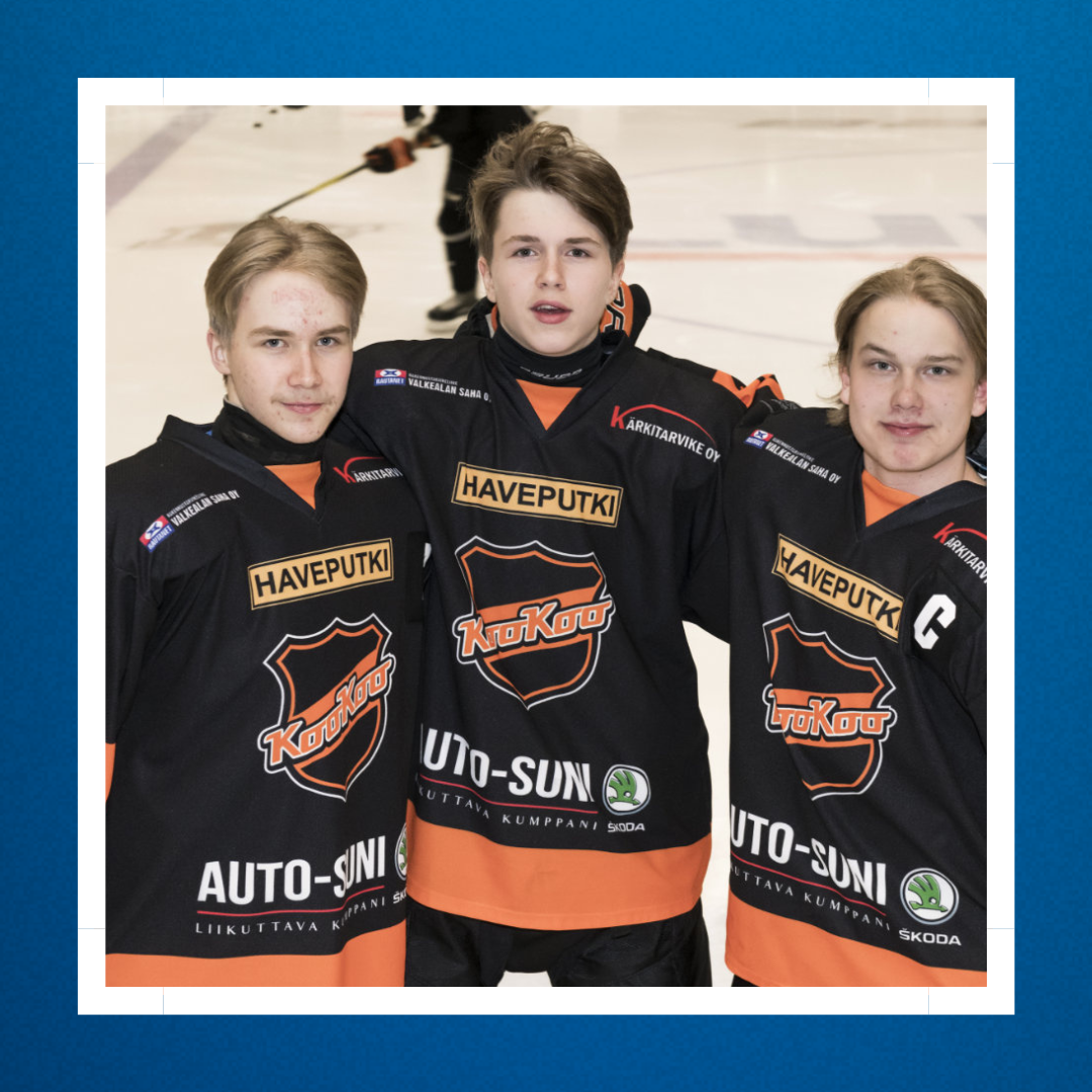 Kolme KooKoo jääkiekkojoukkueen junioripelaajaa seisovat jääkiekkokentällä pitäen käsiä toistensa olkapäillä.